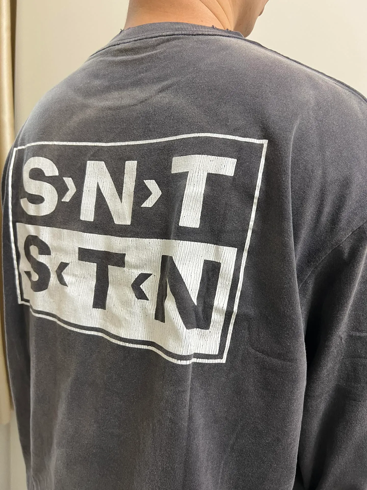 SAINT Mxxxxxx S>N>T LS TEE/BLACK Autumn and winter new style S>N>T slogan crack printed long TEE, washed black S-XL Asut ready-made garments dyed, the whole piece sprayed with horse-hair spray, and then sprayed again to fade the color. The collar and cuffs are frayed. Many hangings are worn NEW VINTAGE. Heavy craftsmanship.